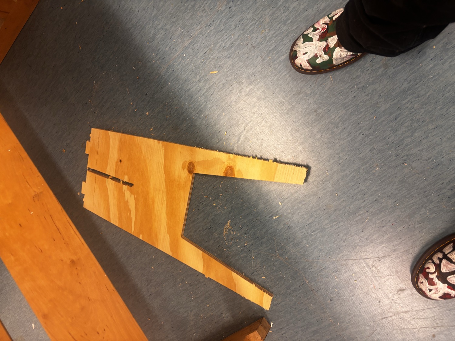 One CNC-milled plywood leg lying on the Fablab floor with visible saw dust around it