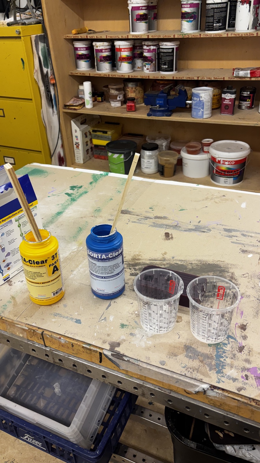 SORTA-Clear 37 part A and part B bottles with stir sticks on a casting room workbench, two empty measuring cups beside them and the wax mold behind