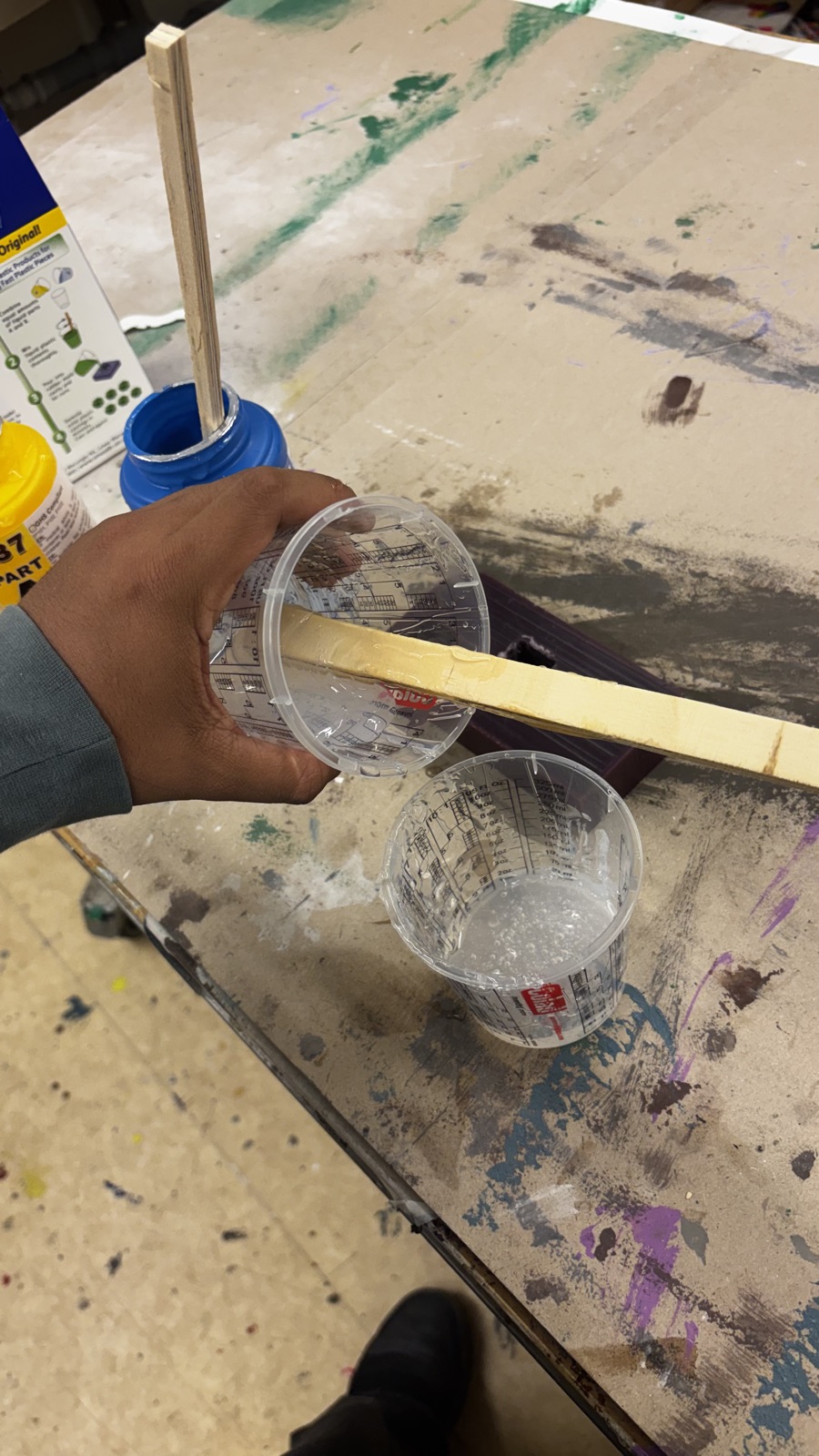 One measuring cup being emptied into the other over the workbench, with the wax mold lying next to them