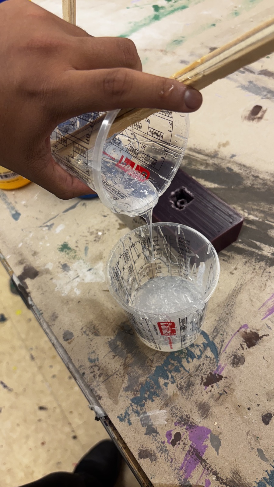 Thick clear silicone stretching in a slow string from one cup into the other