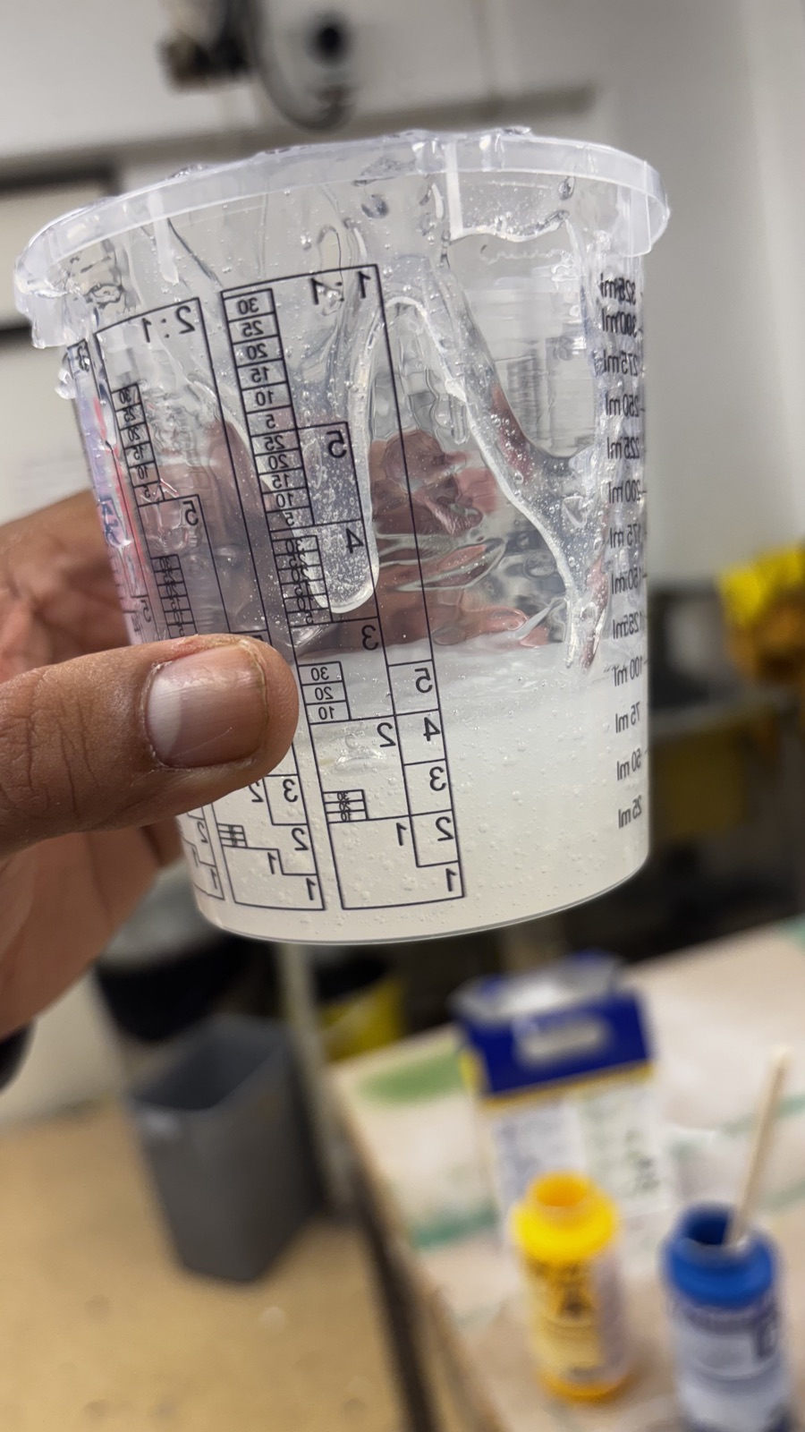 A hand holding the mixing cup with the combined silicone, milky and full of small air bubbles