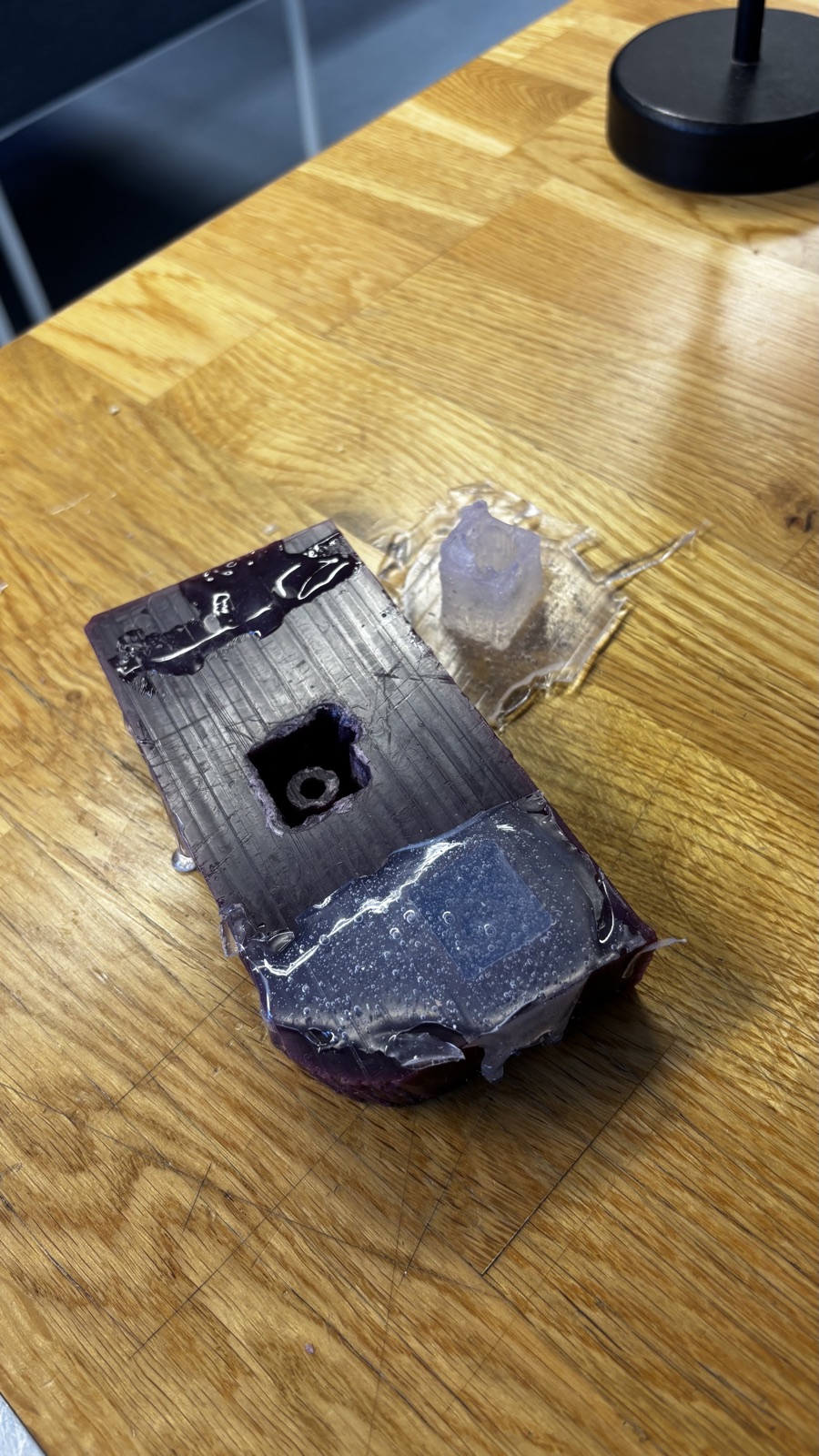 The purple wax block with one cavity already empty and the second silicone piece still in place under its glossy flash, the first demolded mold lying on the table behind it