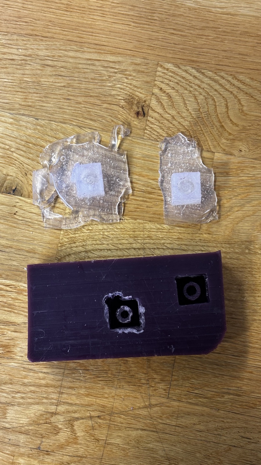 The emptied wax block with both cavities open, and the two demolded silicone pieces with their flash skirts lying above it