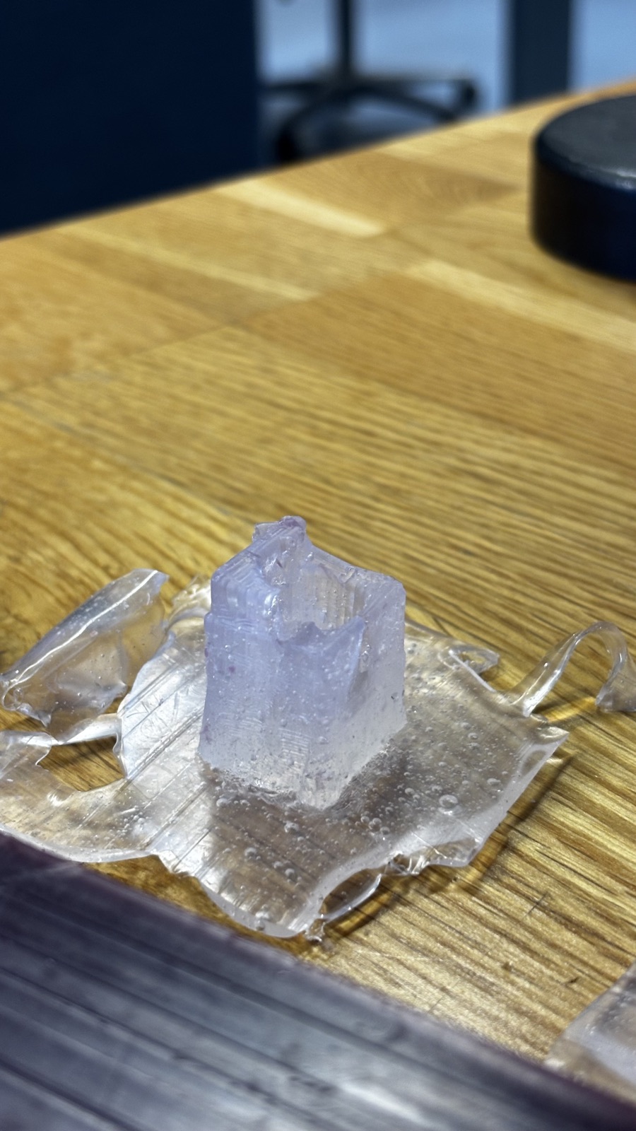 Side view of a silicone mold cube standing on its wrinkled flash skirt, fine horizontal ridges from the milling visible on its walls
