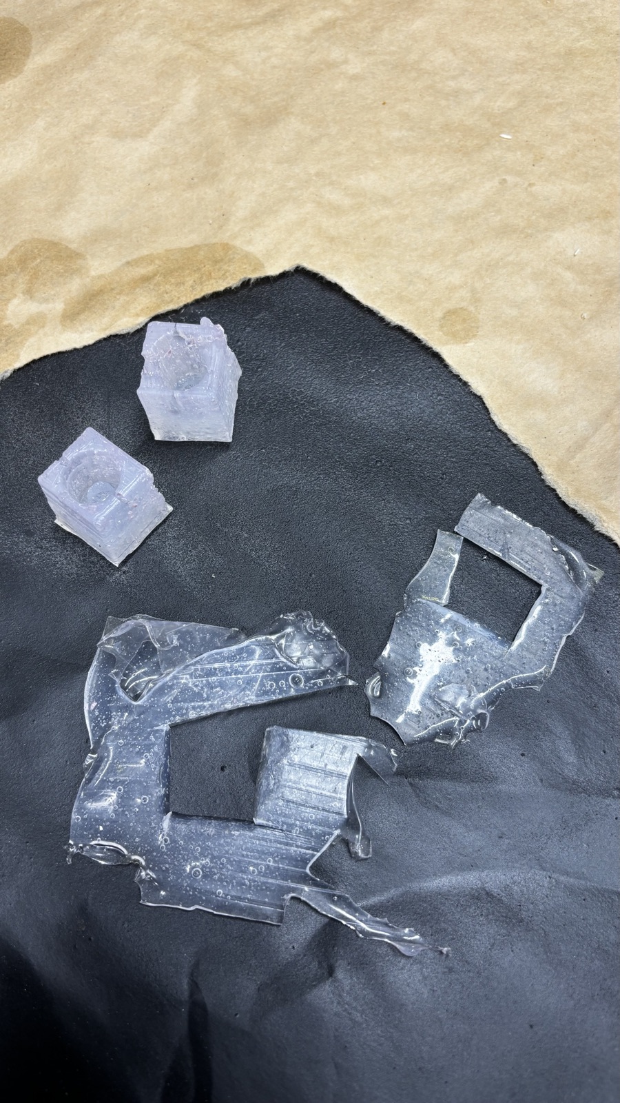 Both trimmed silicone mold cubes on a black mat with the cut away pieces of clear flash lying next to them