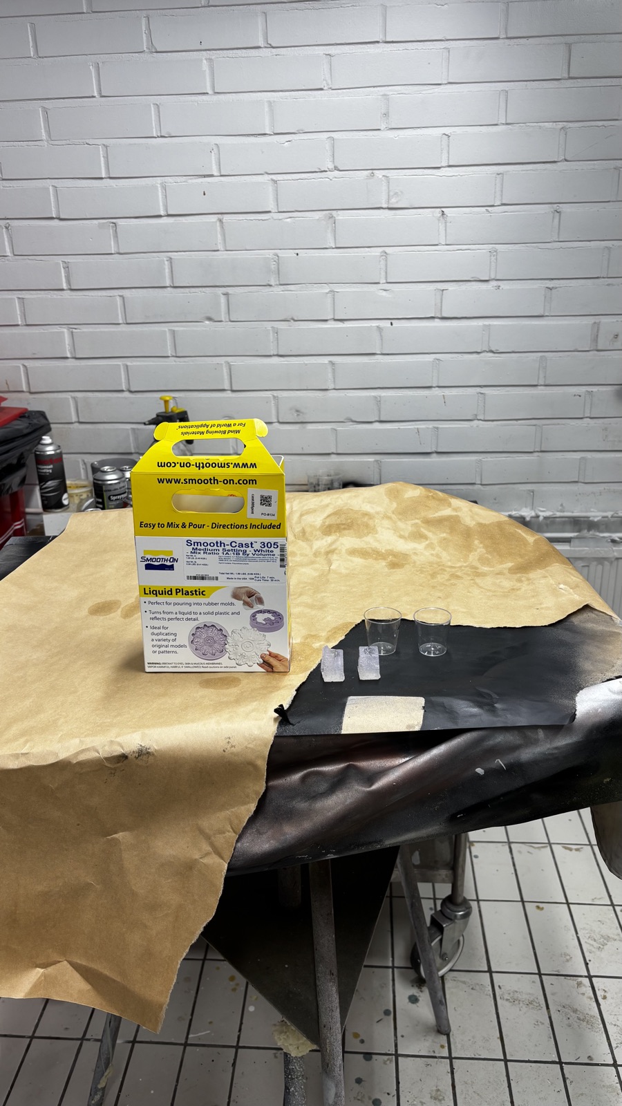 The yellow Smooth-Cast 305 box on the casting room bench with two small mixing cups and the two trimmed silicone molds lined up next to it