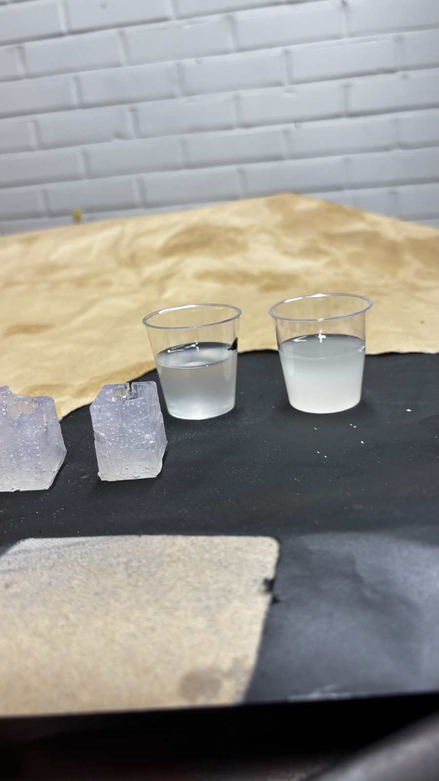 Two small plastic cups with equal amounts of resin, one nearly clear and one milky white, the trimmed molds standing to the left