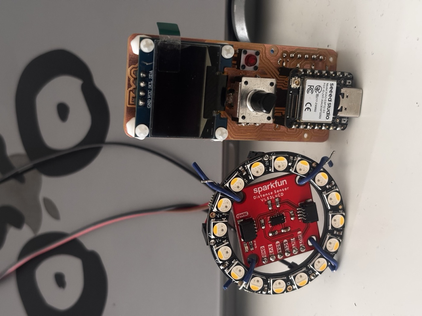Full bench setup showing the milled PCB with the XIAO ESP32-S3, OLED screen, rotary encoder and ToF sensor, with a 12-LED Neopixel ring lit up in red and orange next to it