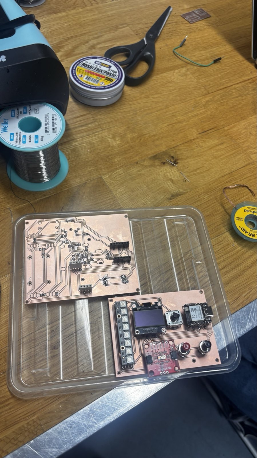Two copper boards in a clear tray: the freshly milled bare receiver board on the left and the populated guitar controller board on the right